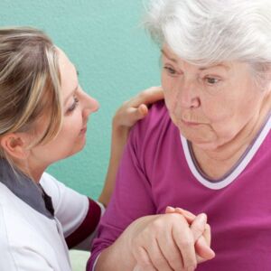 Eine junge hübsche Pflegerin hält einer älteren Dame die Hand.